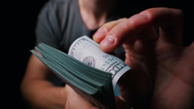 Man hands flip through a thick bundle of one hundred dollar bills against a dark background. Concept of wealth, financial success, greed, corruption, and the power of cash.