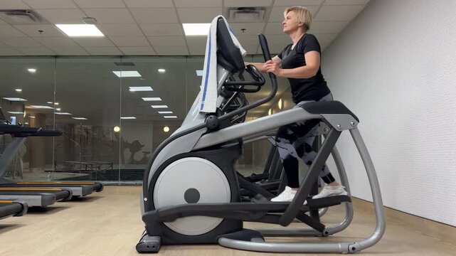 A person is using an elliptical machine in a gym. The workout involves moving arms and legs in a rhythmic manner.