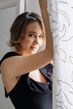 Female portrait. Morning routine. Mindful woman with curtain window in natural light enjoying soft atmosphere comfort lifestyle.