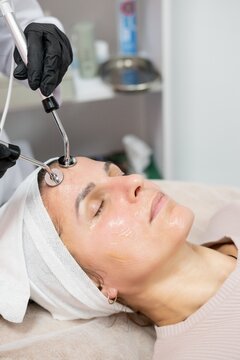 Clinic procedure. Facial therapy. Female beauty master hands in black gloves using professional microcurrent device for skin rejuvenation.