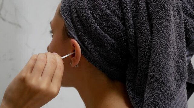 Close-Up of woman cleaning outer ear with cotton swab after shower .