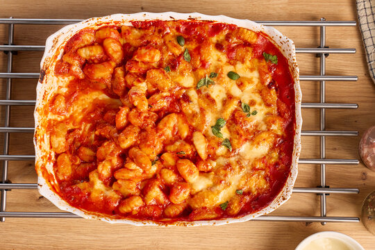 Baked gnocchi with tomato sauce, melted cheese and basil in ceramic dish viewed from above