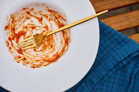 Empty plate with tomato sauce remains and fork on table beside cloth napkin