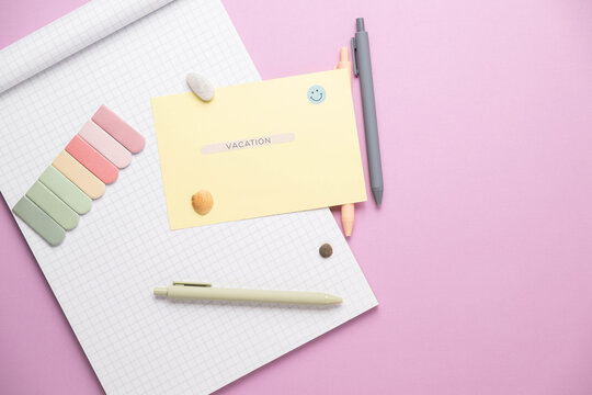 A note pad with blank grid paper on a bright purple background with multicolored sticky note tabs and pastel pens. Written message with word vacation.