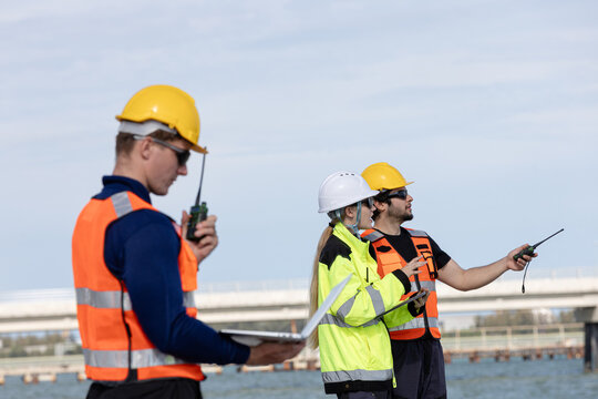 Engineers and construction workers collaborating on a project at a coastal site with safety gear and communication devices
