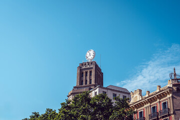 Obraz premium Historic clock tower on ornate building against blue sky in Barcelona
