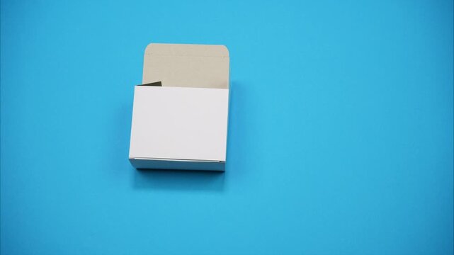 Stop Motion Cardboard Box Folding from Flat Die Cut on Blue Background. Minimal studio footage showing the packaging assembly process