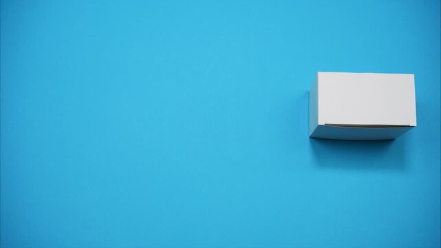 Featuring a blank cardboard die-cut template that appears in the frame, folds into a paper box, and exits the scene on a blue background. Stop motion