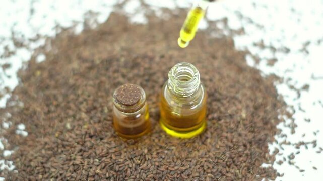 Top View of Flaxseed Oil Glass Bottle with Dropper on Linseeds Pile. Organic Cold Pressed Linseed Oil Dropping from Pipette for Skin Care.