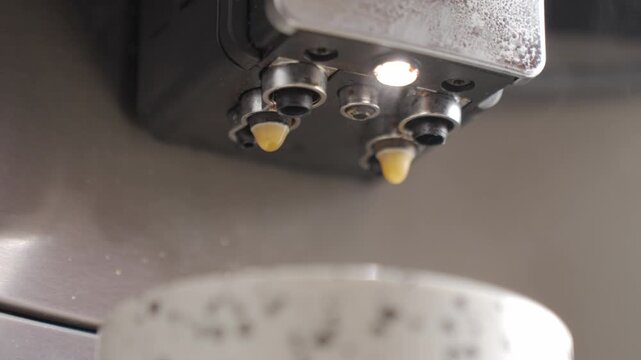 Coffee machine making coffee drink, with streams pouring from nozzles into a cup