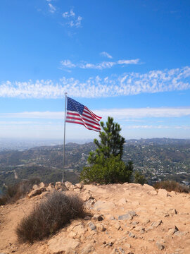 Flag of the United States of America waving on top of Cahuenga Peak at Wisdom Tree with the Hollywood skyline in the background during a summer season in Los Angeles, California, USA