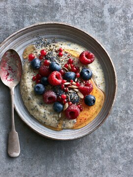 Oatmeal bowl topped with fresh berries and honey on textured background
