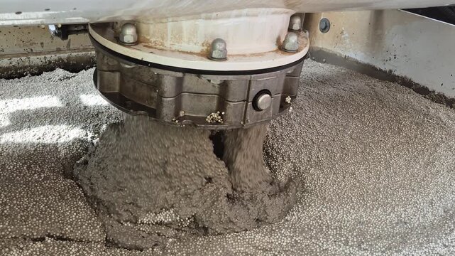 Slow motion close-up of lightweight EPS polystyrene concrete structure pouring into a mixer trough.