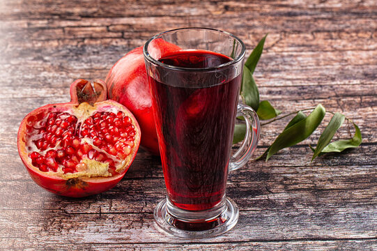 Pomegranate juice in glass mug with fresh pomegranate fruit on rustic wooden table