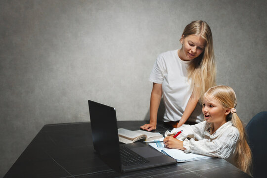 Mother helping her daughter with online school education at home, child reading writing and studying using laptop homeschooling digital distance learning technology, family lifestyle parent and kid