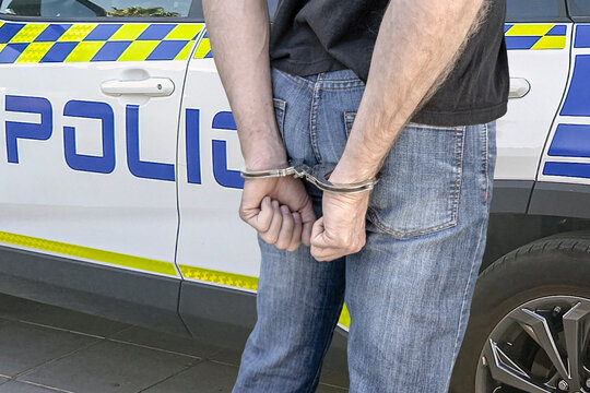 Handcuffed man standing next to a police vehicle