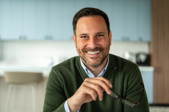 Smiling male professional holding glasses, demonstrating confidence and success, portraying an optimistic attitude in a corporate setting