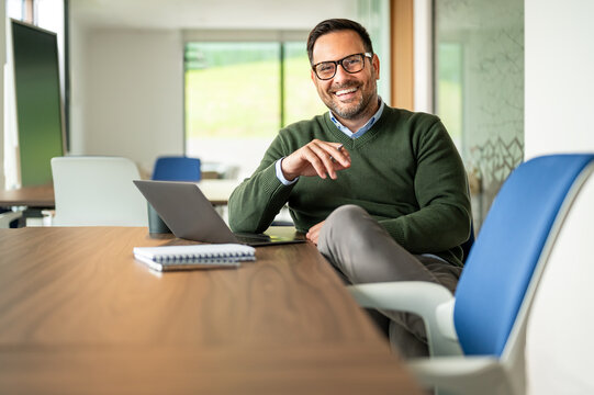 Professional man smiling confidently, creating a positive work environment, showing success and leadership in a modern office working with technology
