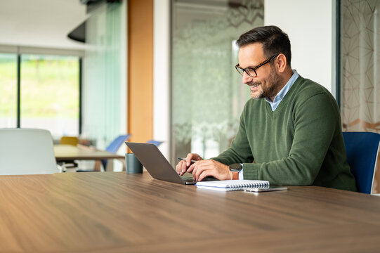Happy businessman in eyeglasses working on a computer in a modern workspace, engaging with technology for business tasks and online communication