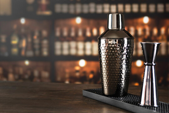 Cocktail shaker and jigger sit on the bar counter. The shaker and jigger are made of gray metal. Concept of a holiday or party. Copy space
