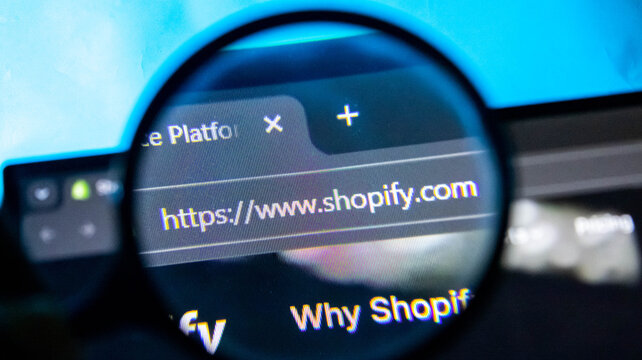Close-up of magnifying glass on Shopify website. E-commerce platform on screen. Online shopping concept.
