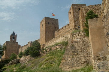 Obraz premium Ancient Alcazaba fortress stone walls and towers with Spanish flag in Antequera, Andalusia, Spain
