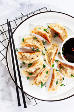 Gyoza, on a white plate,with a sauce pan, a light marble table, no people,