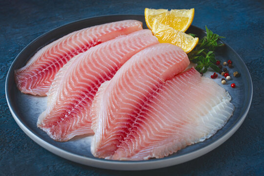 Fresh Tilapia fillet, on a plate, with lemon and herbs, blue background, no people
