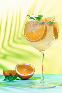 Fresh drink sits on a table near cut oranges with green background and bright light