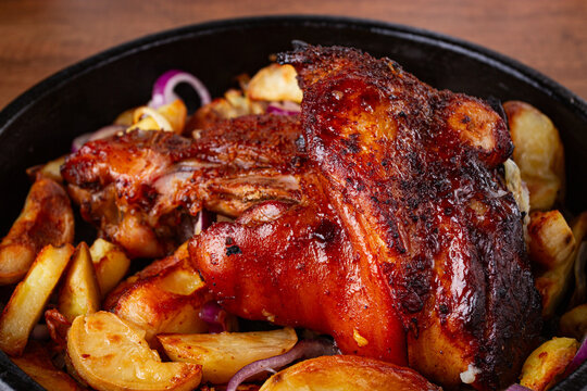 Roasted pork knuckle, with potato slices, on a round pan, on a wooden table, homemade, no people,
