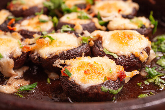 Baked mushrooms with cheese and herbs, laid out in a clay dish,ketzi, Georgian cuisine,on a wooden surface