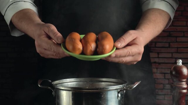 Chef holding green plate with cooked sausages over hot pan in kitchen, rustic brick wall and wooden pepper mill visible in background
