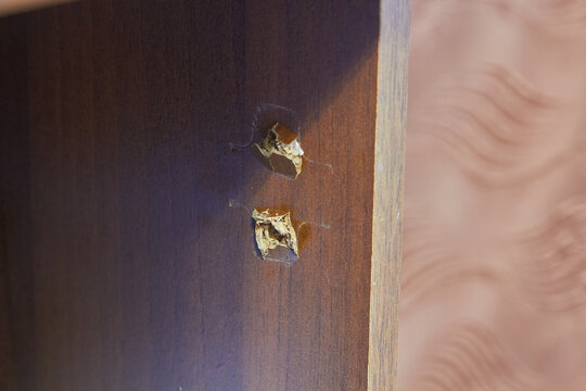 Broken and torn screw holes in a particle board cabinet wall close up, Damaged wooden furniture surface with ripped out dowel or screw holes.