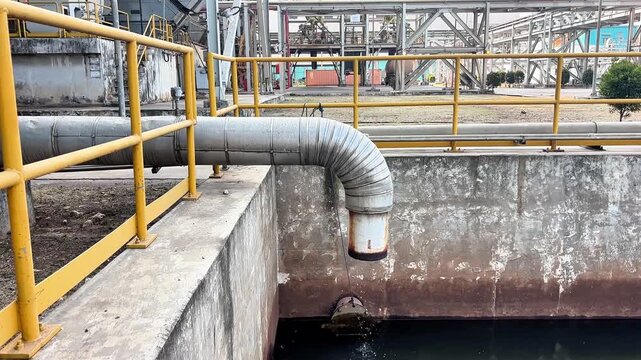 Factory pipe discharges dark waste water into a blowdown concrete basin.