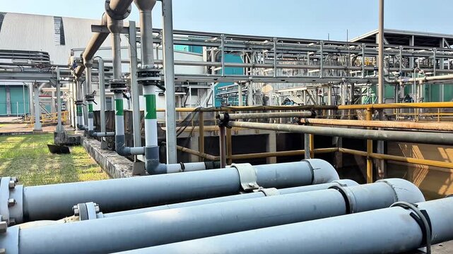 Large drain pipes run beside water treatment basin in industrial plant.