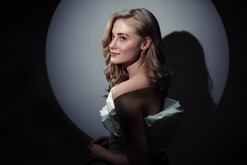 Elegant blonde woman posed in a moody studio portrait with dramatic lighting, soft smile and...