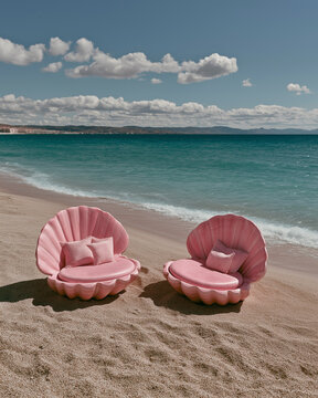 Pink seashell loungers with pillows on a sandy beach near clear water. Ideal for beach resort marketing, coastal lifestyle, and vacation campaigns.