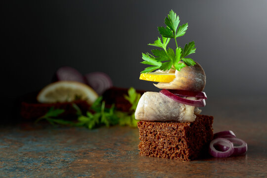 Rye bread canape with herring filet, red onion, lemon, and parsley.
