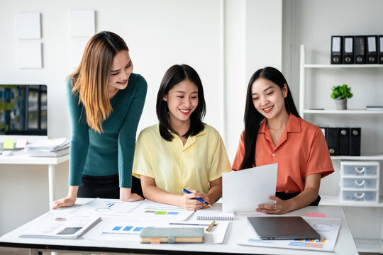 Three women are sitting at a table with papers and a laptop