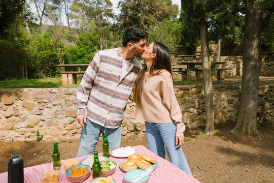 Couple kissing at outdoor picnic table with food and drink
