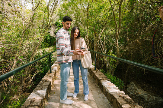 Young couple checking smartphone map on forest footbridge