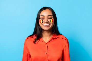 Fototapeta premium Smiling South Asian Woman With Face Paint Representing Country Celebrating Joyfully Against A Blue Background. Expressing Happiness In A Fun And Energetic Manner, Perfect For Celebration Concept.