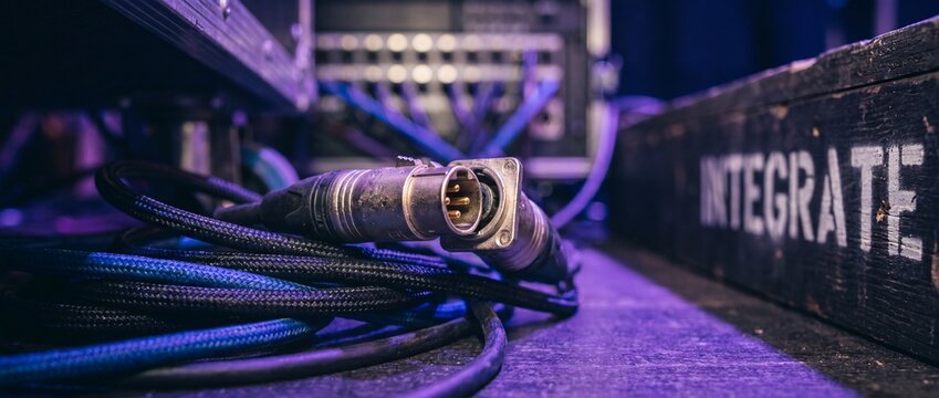 Audio XLR cable stage connector lying on concert backstage floor with purple neon light for professional music sound system setup, live event engineering equipment technology concept close up.