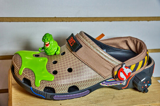Ambato, Ecuador - November 07, 2025: Ghostbusters-themed Crocs shoe with green slime and Slimer character figurine displayed on wooden shelf background