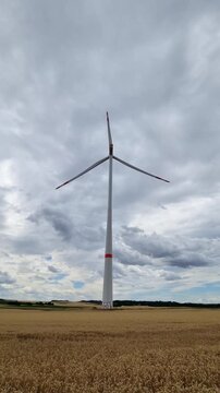 Mainz, Rhineland-Palatinate, Germany: Wind turbine rising above golden wheat field beneath dramatic cloudy sky showcasing renewable energy landscape