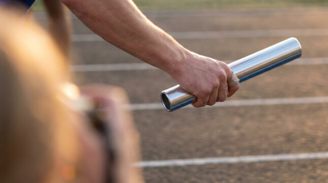 Close-up of athlete's hand holding a metallic relay baton on a running track, symbolizing teamwork and competition