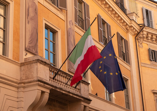 The Italian flag and the EU flag fly together from flagpoles on an beautiful old building in Rome, Italy.