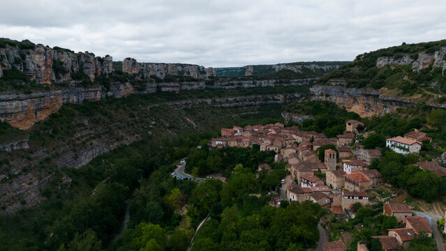 peaceful aerial view of a small village nestled in a canyon surrounded by lush greenery and steep cliffs under a clear sky above stone buildings with wooden roofs.