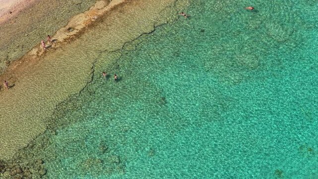 Overhead aerial drone view of crystal-clear turquoise shallows over a rocky reef ledge off Gramvousa island