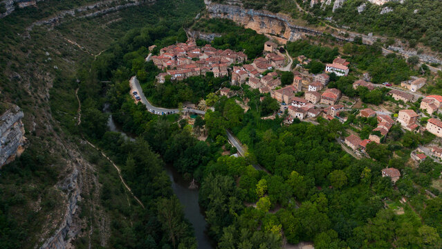 peaceful village nestled in mountainous landscape with river, serene aerial view of stone buildings and wooden roofs on concrete roads, brown and green natural setting with travel and archi.